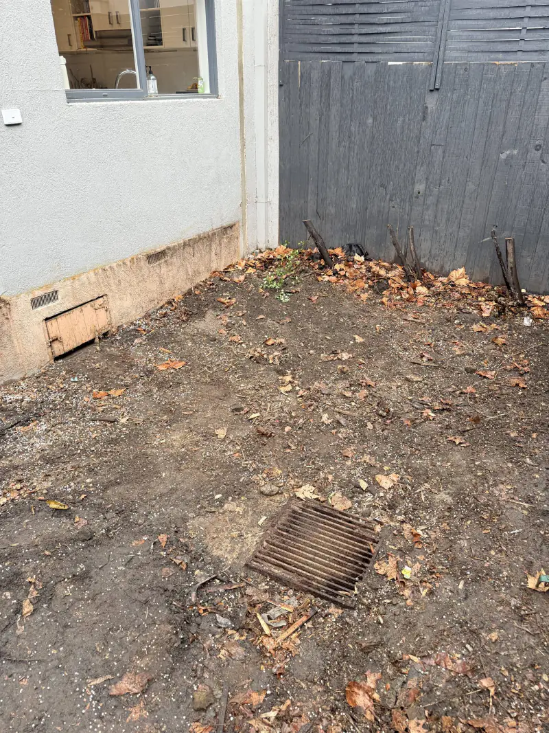 The same side return cleared to bare ground and swept, with the drain cover visible