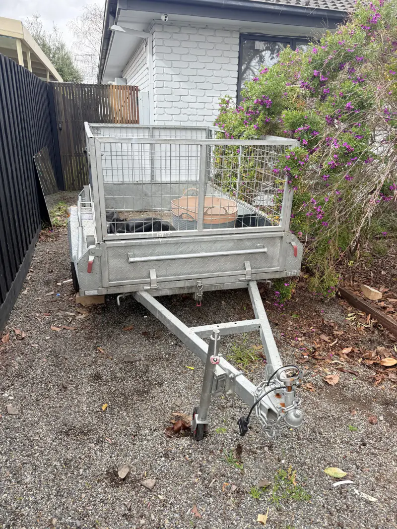 An empty caged trailer parked in a driveway at the start of a rubbish removal job